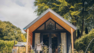 Tiny Loft tiny house met hottub, moderne houten gevel, zonnig terras en groene omgeving met bomen.