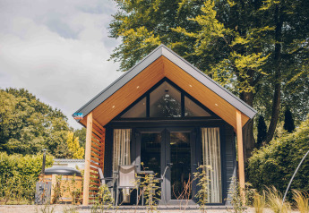 Tiny Loft tiny house with hot tub, modern wooden facade, surrounded by trees and sunny outdoor seating.