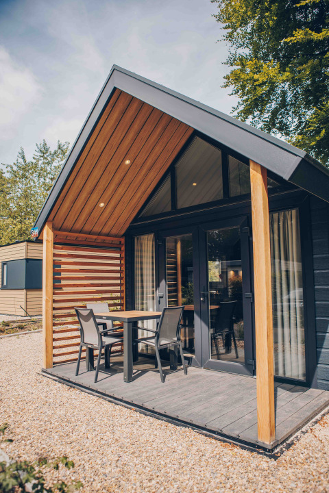 Tiny house moderne avec bardage bois, terrasse couverte, mobilier de jardin et environnement naturel.