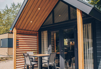 Tiny house moderna con rivestimento in legno, veranda coperta, tavolo e sedie, circondata dalla natura.