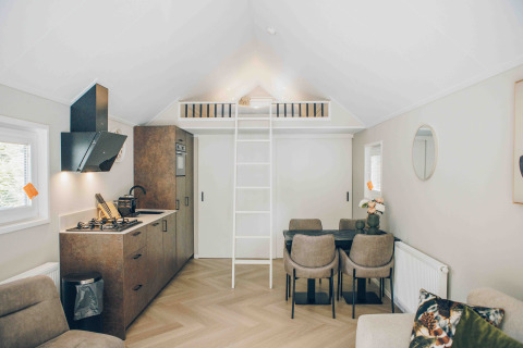 Modern tiny house with a loft bed, compact kitchen, dining area, and cozy decor in light, airy colors.