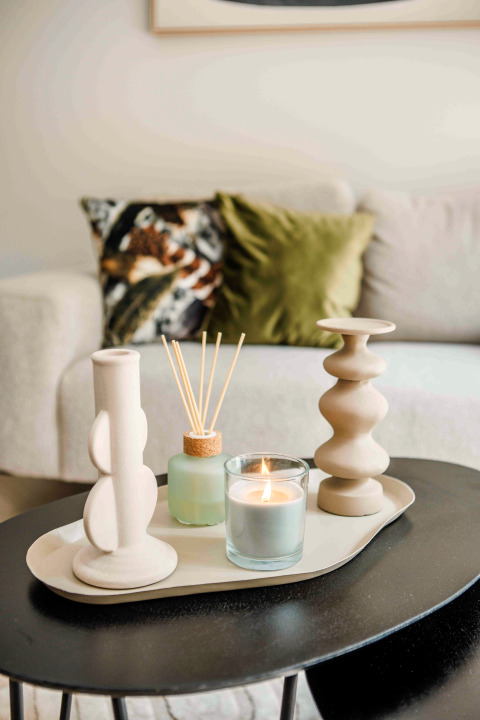 Stylish coffee table in a tiny house featuring a lit candle, diffusers, and decorative vases with cushions behind.