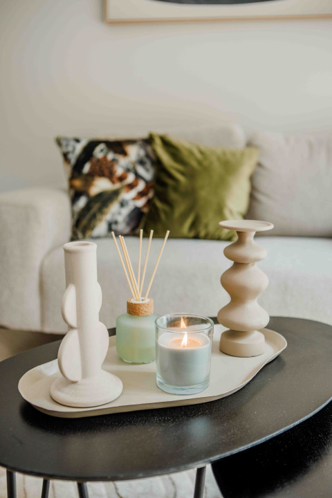 Stylish coffee table in a tiny house featuring a lit candle, diffusers, and decorative vases with cushions behind.