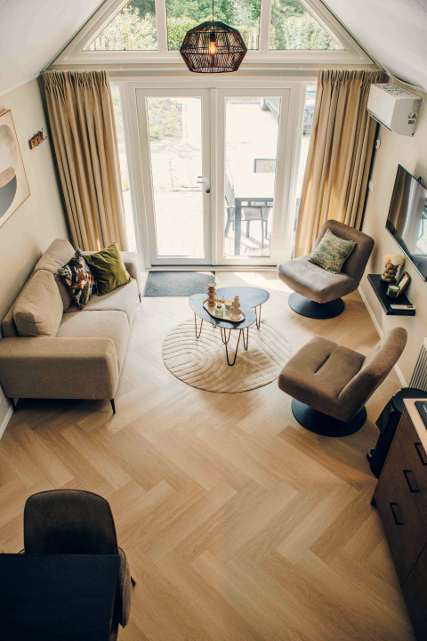 Overhead view of a modern tiny house living room with large windows, cozy seating, and wood flooring.