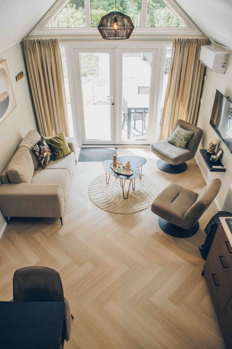 Overhead view of a modern tiny house living room with large windows, cozy seating, and wood flooring.