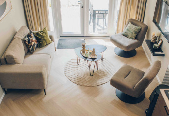 Vista aérea de una sala moderna en una tiny house con amplios ventanales, sofá y suelos de madera.