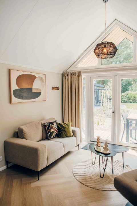 Salon douillet dans une tiny house avec canapé beige, art moderne, tables rondes et vue sur le jardin.