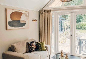 Gezellige woonkamer in een tiny house met beige bank, moderne kunst, ronde tafels en tuinzicht.