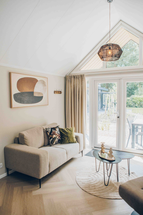 Cozy living room in a tiny house featuring a beige sofa, modern art, round tables, and garden views.