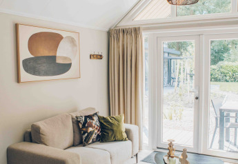 Gemütliches Wohnzimmer im Tiny House mit beiger Couch, moderner Kunst und Blick durch große Fenster.