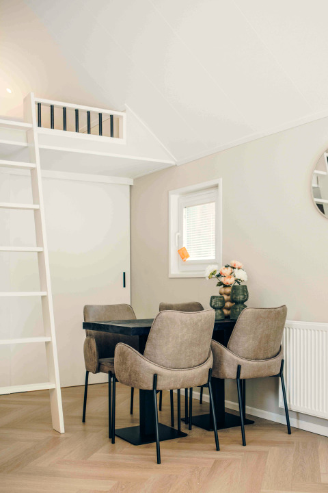 A small modern dining area in a tiny house with four chairs, a black table, a ladder, and loft space.