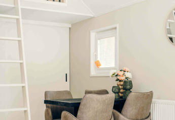 Kleine moderne eethoek in een tiny house met vier stoelen, zwarte tafel, ladder en mezzanine.