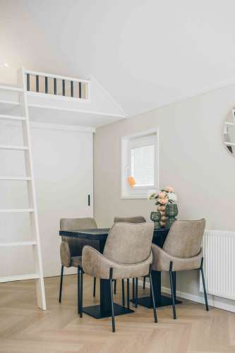 Pequeño comedor moderno en una tiny house con cuatro sillas, mesa negra, escalera y altillo.