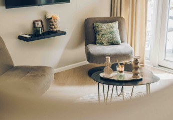 Soggiorno moderno in una tiny house con poltrone accoglienti, tavolino decorativo e molta luce naturale.
