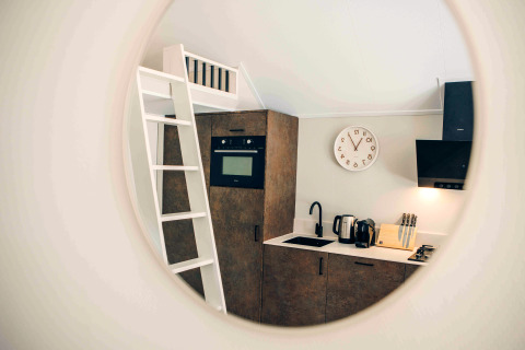 Vue dans un miroir d'une petite cuisine de tiny house avec échelle, four, évier et bloc de couteaux.