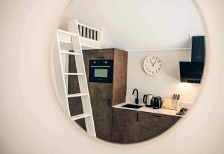 Vue dans un miroir d'une petite cuisine de tiny house avec échelle, four, évier et bloc de couteaux.