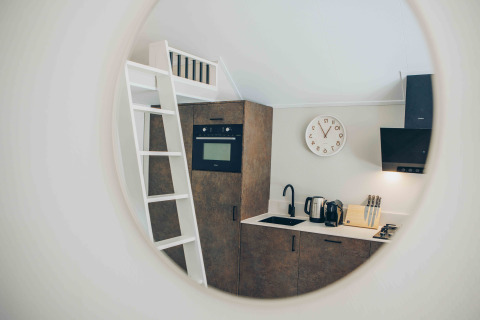Mirror view of a compact tiny house kitchen with a ladder, oven, sink, kettle, and knife block.