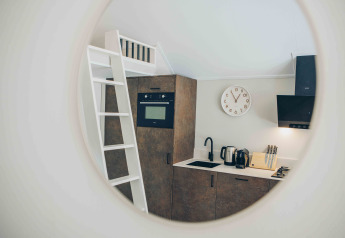 Mirror view of a compact tiny house kitchen with a ladder, oven, sink, kettle, and knife block.