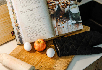 Cocina en mini casa con libro de recetas, manzana, huevos, rodillo y guante de horno sobre una tabla.