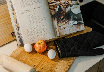 Küchenszene im Tiny House mit Kochbuch, Apfel, Eiern, Teigrolle und Topfhandschuh auf dem Brett.