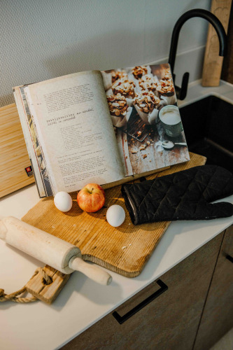 Küchenszene im Tiny House mit Kochbuch, Apfel, Eiern, Teigrolle und Topfhandschuh auf dem Brett.