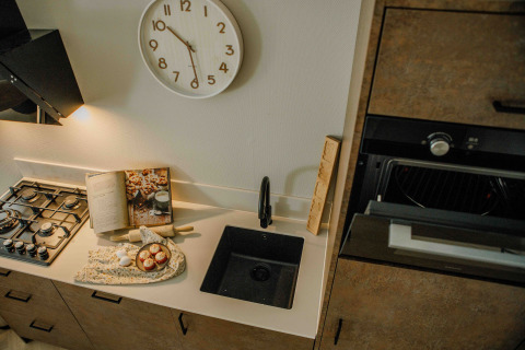 Cucina compatta in una tiny house con fornello a gas, lavello nero, libro di cucina e orologio da parete.