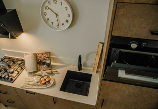 Kleine, moderne keuken in een tiny house met gaskookplaat, spoelbak, oven en bakbenodigdheden.