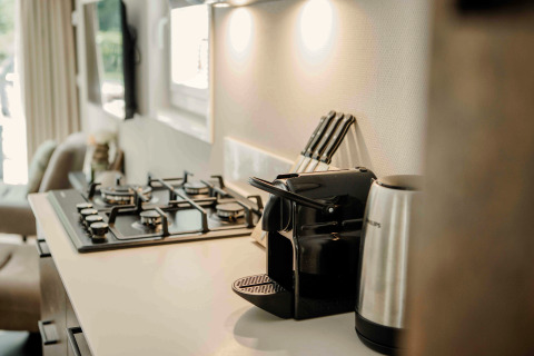 Modern kitchenette in a tiny house featuring a gas stove, coffee machine, kettle, and a knife set.