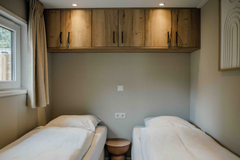 Deux lits simples dans une chambre de tiny house, avec placards en bois, fenêtre et lumière tamisée.