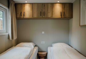 Due letti singoli in una tiny house con mobili pensili in legno, finestra e illuminazione soffusa.