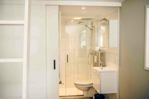 Bright, compact bathroom in a tiny house featuring a shower, toilet, and sink with modern white decor.