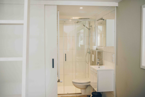 Bright, compact bathroom in a tiny house featuring a shower, toilet, and sink with modern white decor.