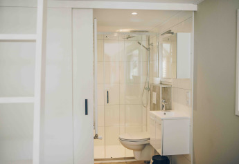 Bagno compatto e luminoso in una tiny house, con doccia, WC e lavabo in arredo bianco moderno.