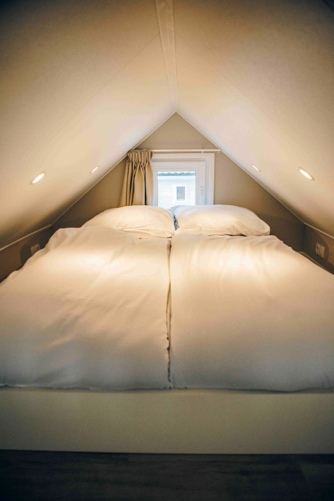 Cozy sleeping loft in a tiny house with a double bed, soft lighting, and a small window at the end.