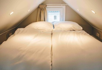 Accogliente zona notte in una tiny house con letto matrimoniale, soffitto basso e piccola finestra.