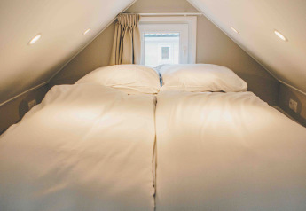 Gemütliche Schlafnische in einem Tiny House mit Doppelbett, niedriger Decke und kleinem Fenster.