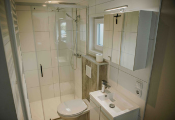 Salle de bain moderne et compacte dans une tiny house avec douche, toilettes, lavabo et armoire miroir.