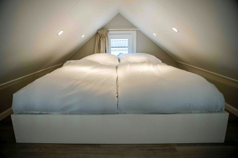 Petite chambre sous combles dans une tiny house avec lit double et couettes blanches douces.