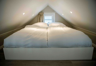 A tiny house loft bedroom with a double bed and soft white duvets placed under an angled ceiling.