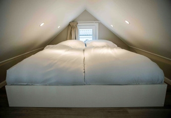 Dormitorio en altillo de una tiny house con cama doble y edredones blancos bajo un techo inclinado.