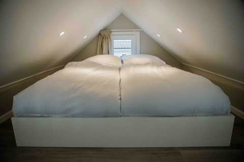 Dormitorio en altillo de una tiny house con cama doble y edredones blancos bajo un techo inclinado.