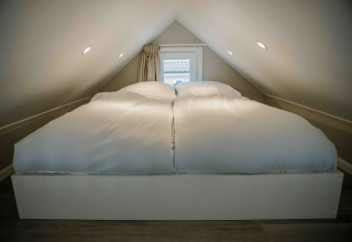 Slaapkamer in een tiny house met een tweepersoonsbed en witte dekbedden onder een schuin plafond.