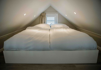 A tiny house loft bedroom with a double bed and soft white duvets placed under an angled ceiling.