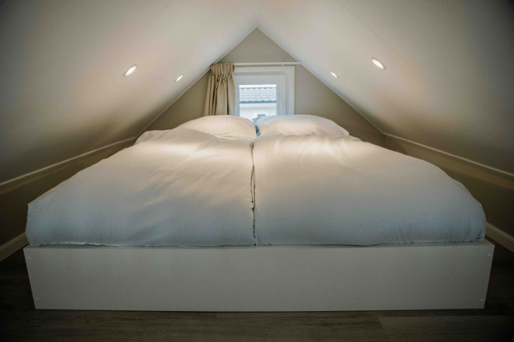 Dormitorio en altillo de una tiny house con cama doble y edredones blancos bajo un techo inclinado.