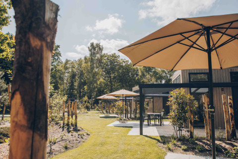 Terrazza all'aperto con grandi ombrelloni e lodge moderno al Reeëndal Lodge Comfort, Veluwepark de Bosgraaf.