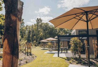 Außenterrasse mit großen Sonnenschirmen und moderner Lodge bei Reeëndal Lodge Comfort im Veluwepark de Bosgraaf.