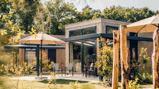 Außenaufnahme der Reeëndal Lodge mit moderner Holzfassade, großen Fenstern und Sonnenschirmen im Garten.