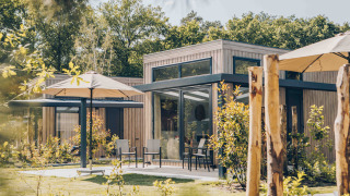 Buitenaanzicht van Reeëndal Lodge met moderne houten gevel, grote ramen en parasols in een groene tuin.