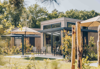 Vista esterna di Reeëndal Lodge con facciata in legno moderno, ampie finestre e ombrelloni nel giardino verde.