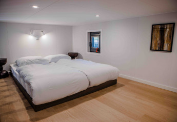 Moderne soveværelse på en lodge med dobbeltseng, hvidt sengetøj, minimalistiske møbler og kunst på væggen.